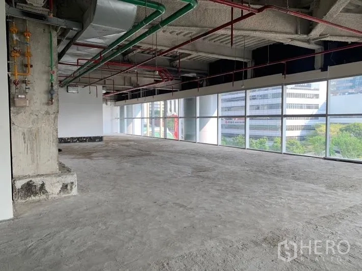 Retail Space for rent - Open-plan unit with city and tree views through full-height glass and visible MEP services.