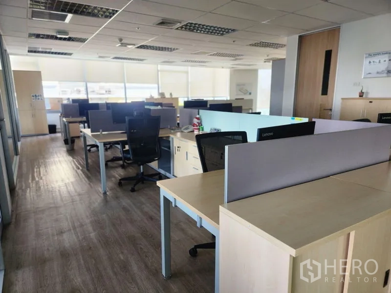 Office Space for rent - Long aisle of shared desks and office chairs with daylight and light wood furniture.
