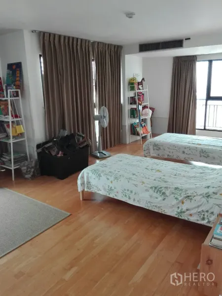 Condominium for rent in Khlong Toei, Bangkok - Large twin bedroom with windows, full-length curtains, bookshelves and warm wood flooring.