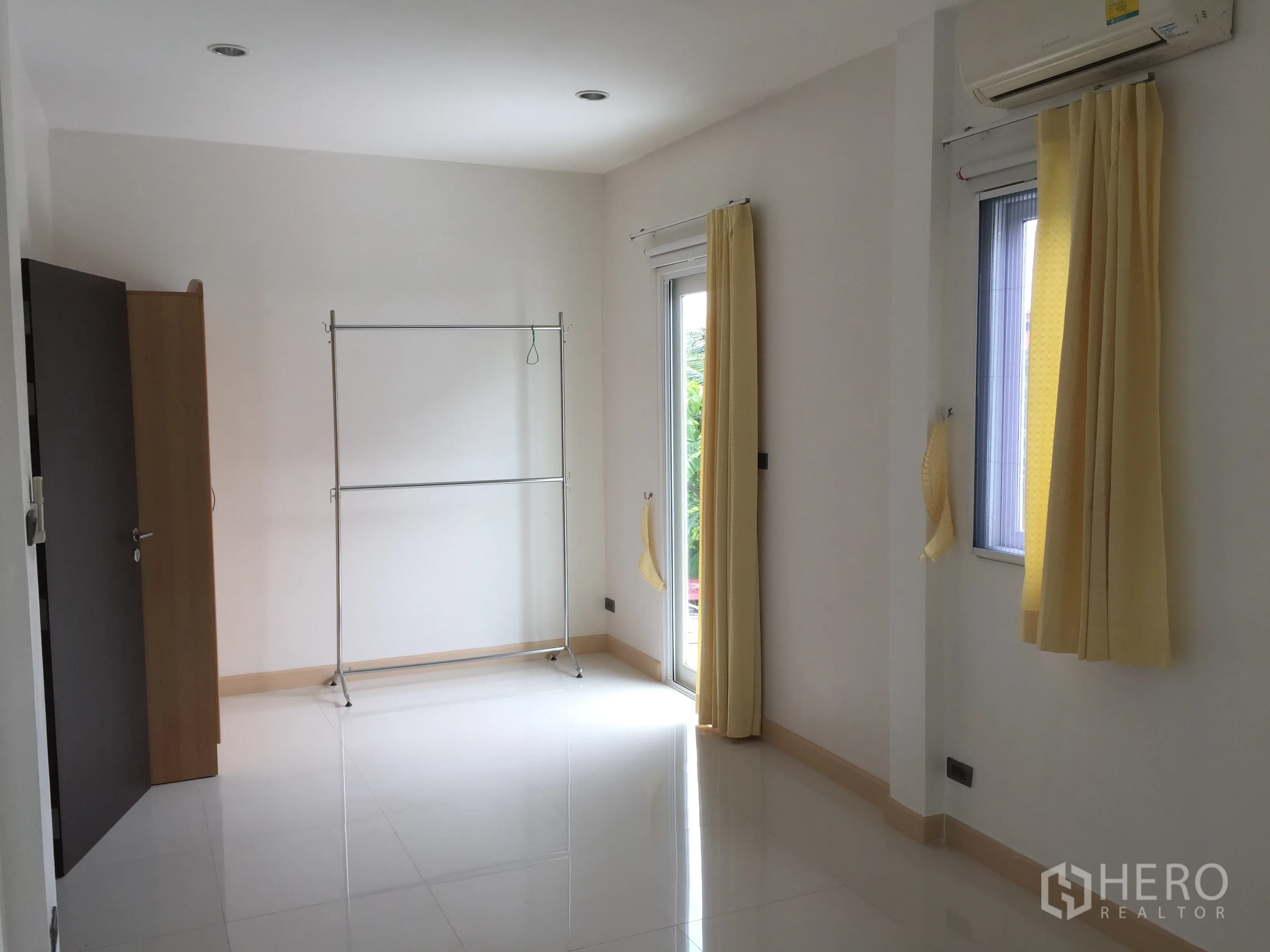 Townhouse for rent in Din Daeng, Bangkok - Spacious white room with yellow curtains, split air-conditioner and a door to the balcony.