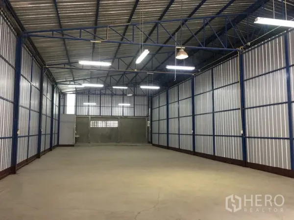 Warehouse for rent in Bang Kapi, Bangkok - Clear-span warehouse with steel truss ceiling, corrugated metal walls, fluorescent lighting and a rear loading door for efficient operations.