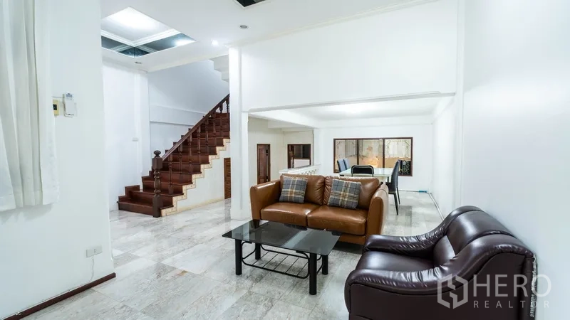 Townhouse for rent in Khlong Toei, Bangkok - Open‑plan living area with marble floors, leather sofas and a wooden staircase.