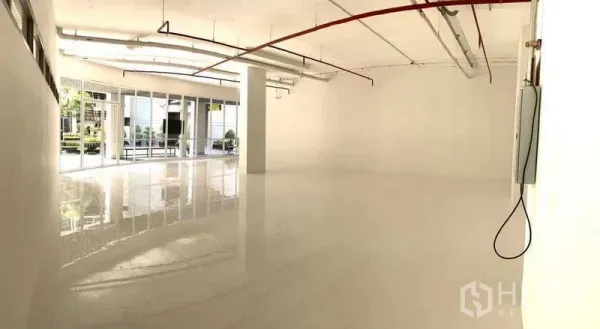 办公空间 出租在Khlong Toei, Bangkok - 通透明亮的开放式办公室，白色亮面地砖，裸露天花灯具与管线，整面落地玻璃正对绿化中庭。