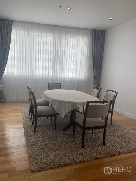 Condominium for rent in Khlong Toei, Bangkok - Dining area with a six-seat round table, soft curtains and a wide window.