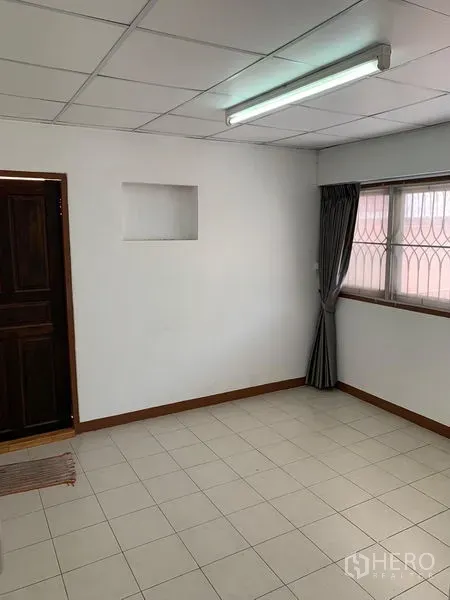 Office Space for rent in Chatuchak, Bangkok - Bright room with white tiled floor, curtained window with security grille and fluorescent light.