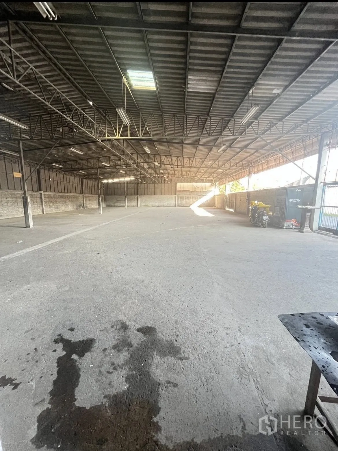 Warehouse for rent in Chatuchak, Bangkok - Covered warehouse area with wide concrete floor and lighting looking toward the entrance.