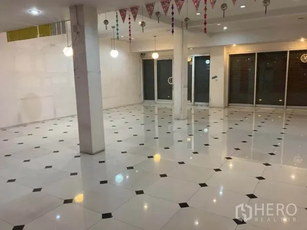 Shophouse for rent in Suan Luang, Bangkok - Open-plan shophouse interior with glossy white tiled floor, pillars, pendant lights and a wide glass frontage with shutters.