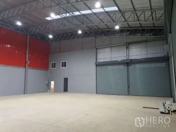 Warehouse for rent in Khlong Luang, Pathum Thani - Open warehouse floor with red wall panels, two large roller shutter doors and a compact internal office.