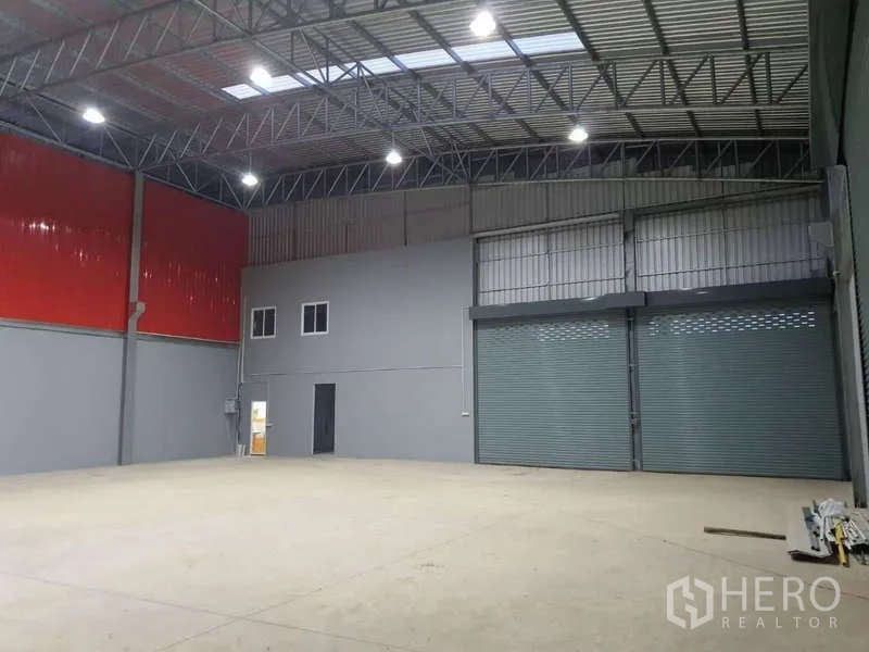 Warehouse for rent in Khlong Luang, Pathum Thani - Open warehouse floor with red wall panels, two large roller shutter doors and a compact internal office.