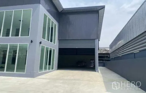 Warehouse for rent in Prawet, Bangkok - Covered loading area with large roller shutter beside the glass office wing and wide driveway for trucks.