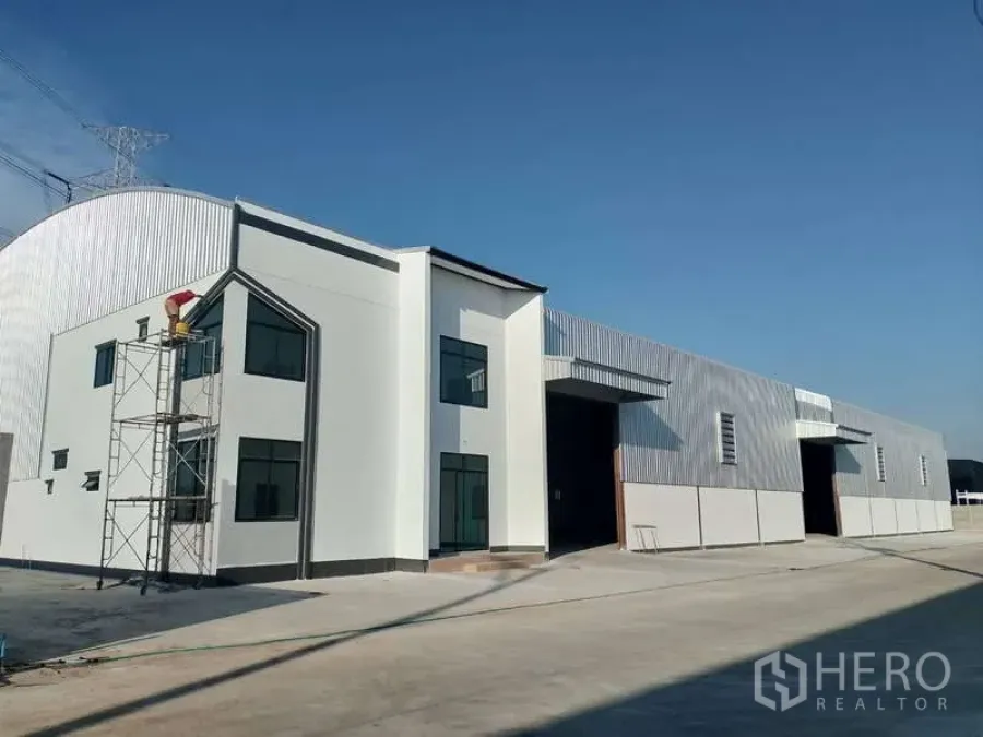 Factory for rent or sale in Sai Noi, Nonthaburi - New factory exterior with attached two-storey office block, wide roller shutter and concrete yard under a clear blue sky.