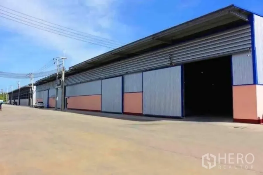 Warehouse for rent in Mueang Samut Sakhon, Samut Sakhon - Warehouse exterior showing large sliding metal doors, sheltered loading area and ample apron for trucks.