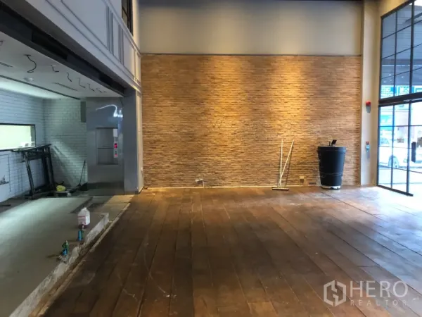 Retail Space for rent in Khlong Toei, Bangkok - Open-plan retail area with brick feature wall, warm wall lighting, and hardwood floors near the shopfront.
