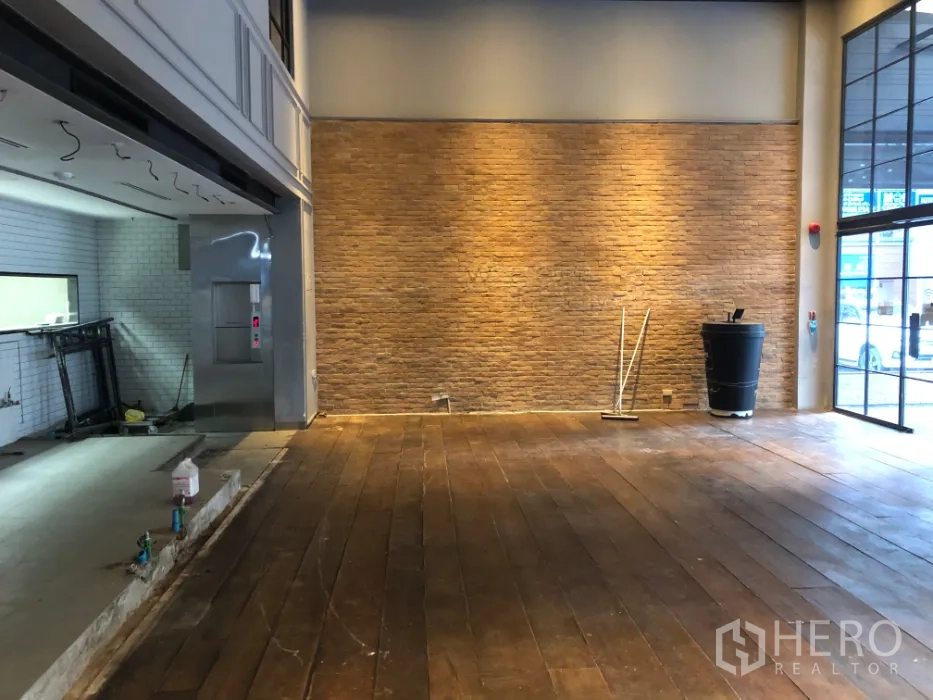 Retail Space for rent in Khlong Toei, Bangkok - Open-plan retail area with brick feature wall, warm wall lighting, and hardwood floors near the shopfront.