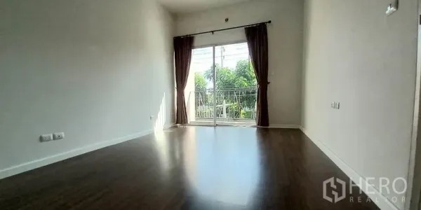 Townhouse for sale in Mueang Pathum Thani, Pathum Thani - Bright upper-floor room with wood flooring and sliding glass door to a small balcony.