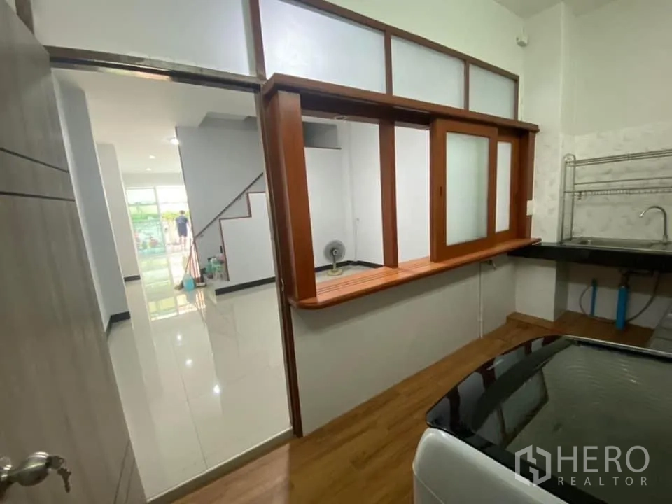 Townhouse for rent in Huai Khwang, Bangkok - Closed kitchen with pass-through window, sink, black countertops, and appliance space.