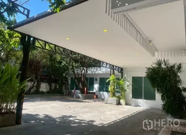 Home Office for rent in Watthana, Bangkok - Covered carport with downlights and a wide driveway bordered by mature greenery.