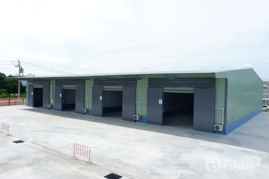 Warehouse for rent in Pak Kret, Nonthaburi - Row of new warehouse units with wide roller doors and a large truck-friendly concrete yard.