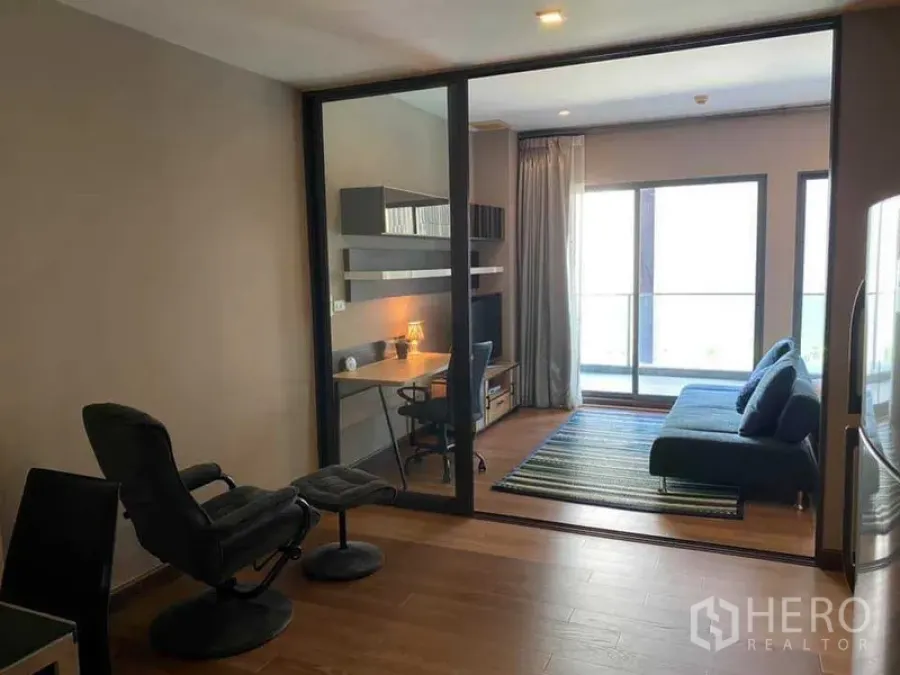 Condominium for rent in Khlong Toei, Bangkok - Glass-partitioned living room with blue sofa, study desk, and balcony doors in a modern Bangkok condo.