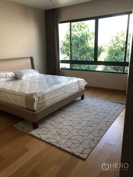 Detached House for rent or sale in Huai Khwang, Bangkok - Sunlit bedroom with a large window, green views, wood floors and an upholstered bed.