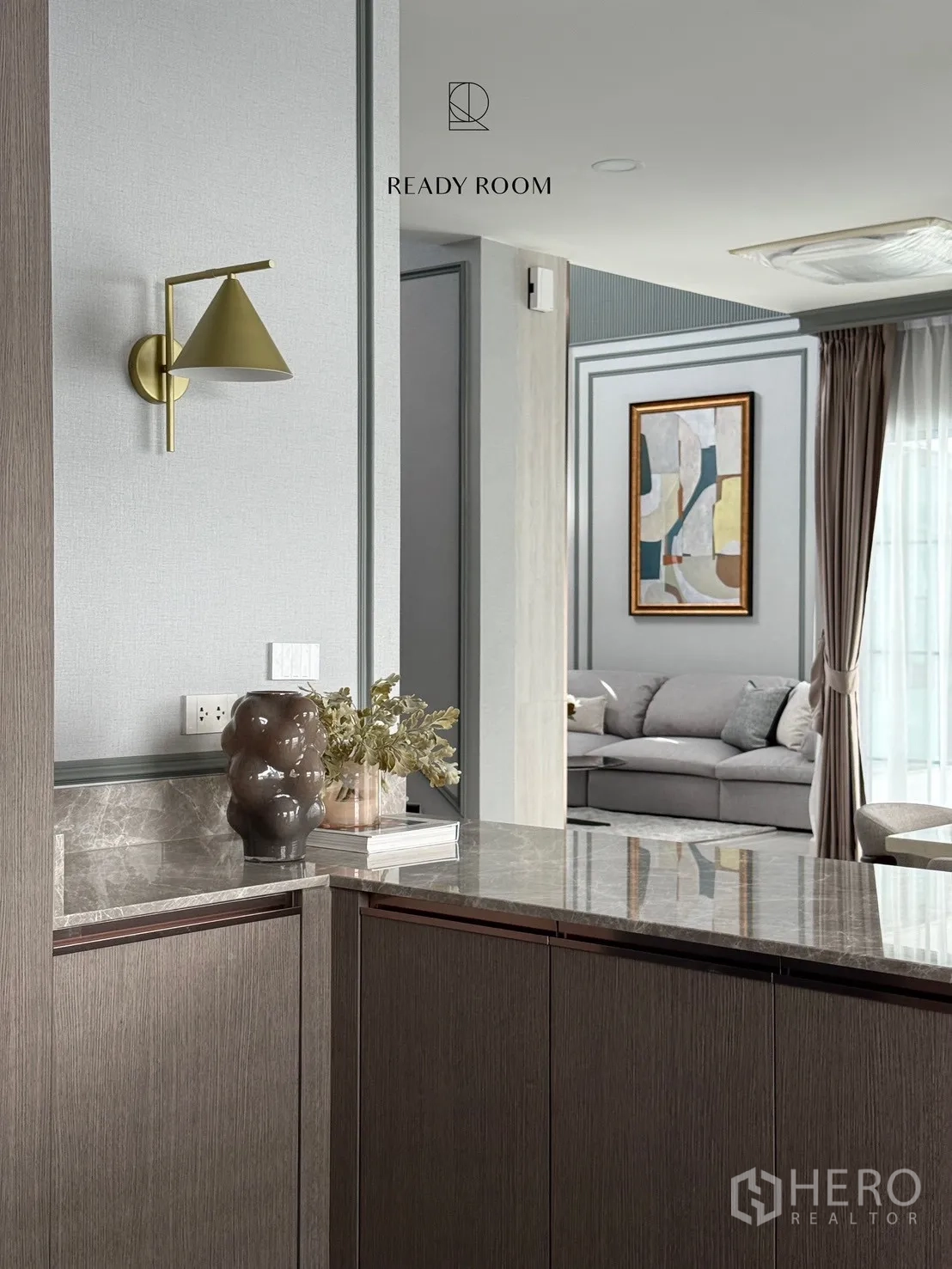 Detached House for rent or sale in Bang Phli, Samut Prakan - Close-up of marble breakfast bar with brass wall sconce and a view toward the grey sofa living area.
