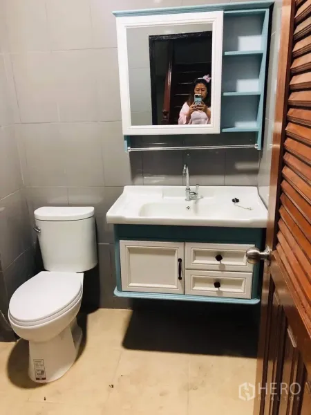 Townhouse for rent or sale in Huai Khwang, Bangkok - Modern bathroom with toilet, vanity sink, mirrored cabinet and tiled walls.