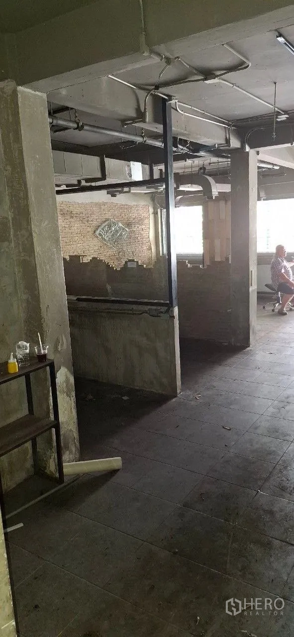 Shophouse for rent or sale in Watthana, Bangkok - Open-plan floor with concrete columns, exposed ventilation ducts, and half-height brick partitions.
