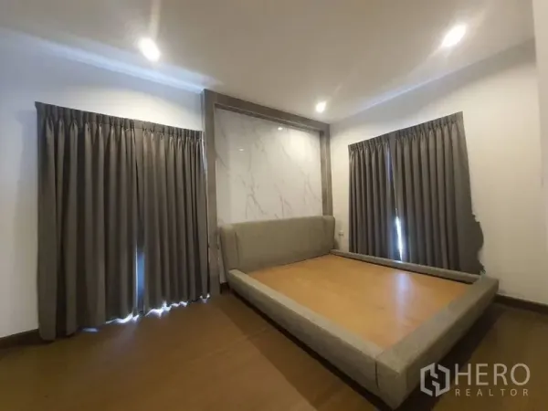Detached House for rent in Prawet, Bangkok - Bedroom with platform bed frame, marble feature wall, wood floor and dark curtains.