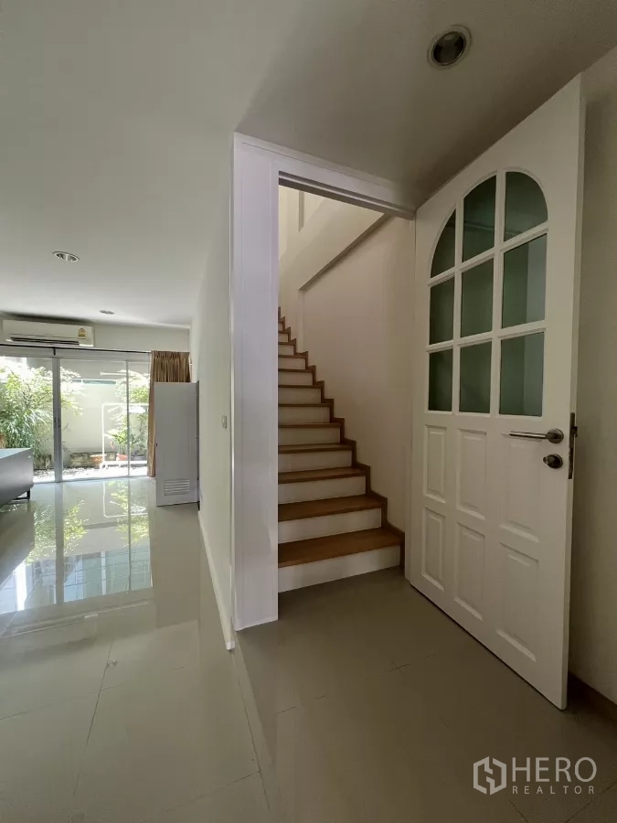 Townhouse for rent in Suan Luang, Bangkok - Close view of the staircase and white door off the living area with glossy floor tiles.