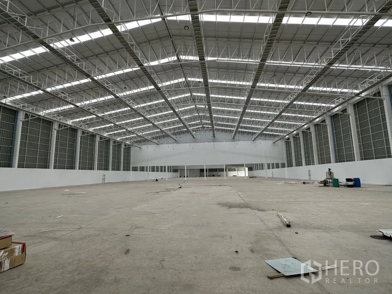 Factory for rent in Pathum Thani - Expansive high-bay warehouse hall with a steel truss roof and ventilated windows.