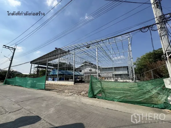 Warehouse for rent in Bang Kapi, Bangkok - Warehouse steel frame under construction along a local street with power lines and green safety netting.