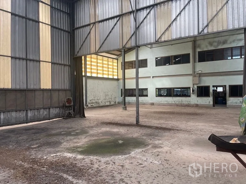 Warehouse for rent or sale in Bang Bon, Bangkok - Covered work bay facing internal office windows and a large opening.