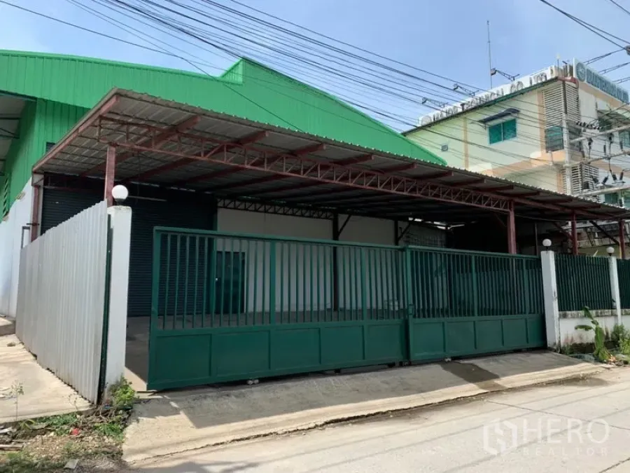 Factory for rent in Pathum Thani - Gated factory exterior with green roof, covered loading bay and sliding metal gate.