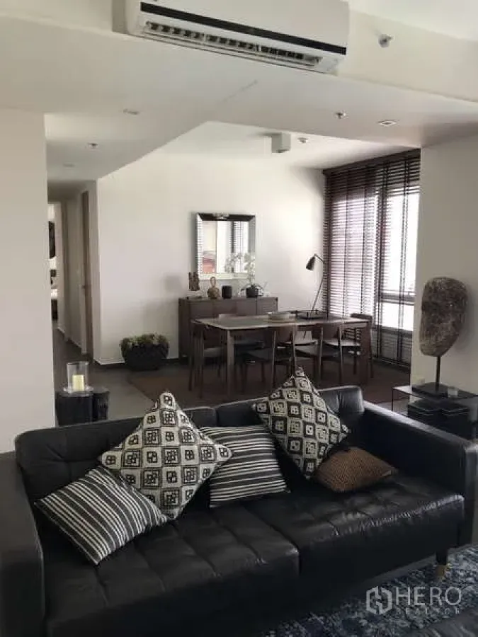 Condominium for sale in Watthana, Bangkok - Stylish living room with black leather sofa, dining set and full-height windows with blinds.