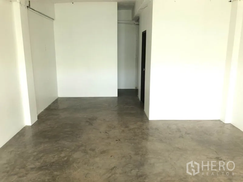 Retail Space for rent in Khlong Toei, Bangkok - White-walled shop space with concrete flooring and a doorway leading to the back area and bathroom.