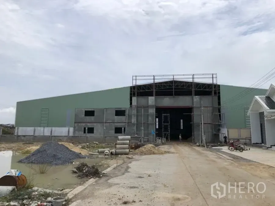 คลังสินค้า ให้เช่าหรือขายในSai Noi, Nonthaburi - ด้านหน้าโกดังโครงเหล็กขนาดใหญ่กำลังก่อสร้าง มีประตูทางเข้ากว้างและถนนภายใน