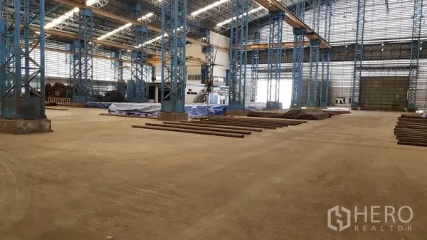Factory for rent in Mueang Samut Sakhon, Samut Sakhon - Open manufacturing area with blue steel columns, heavy‑duty concrete floor, and large roller shutter doors.