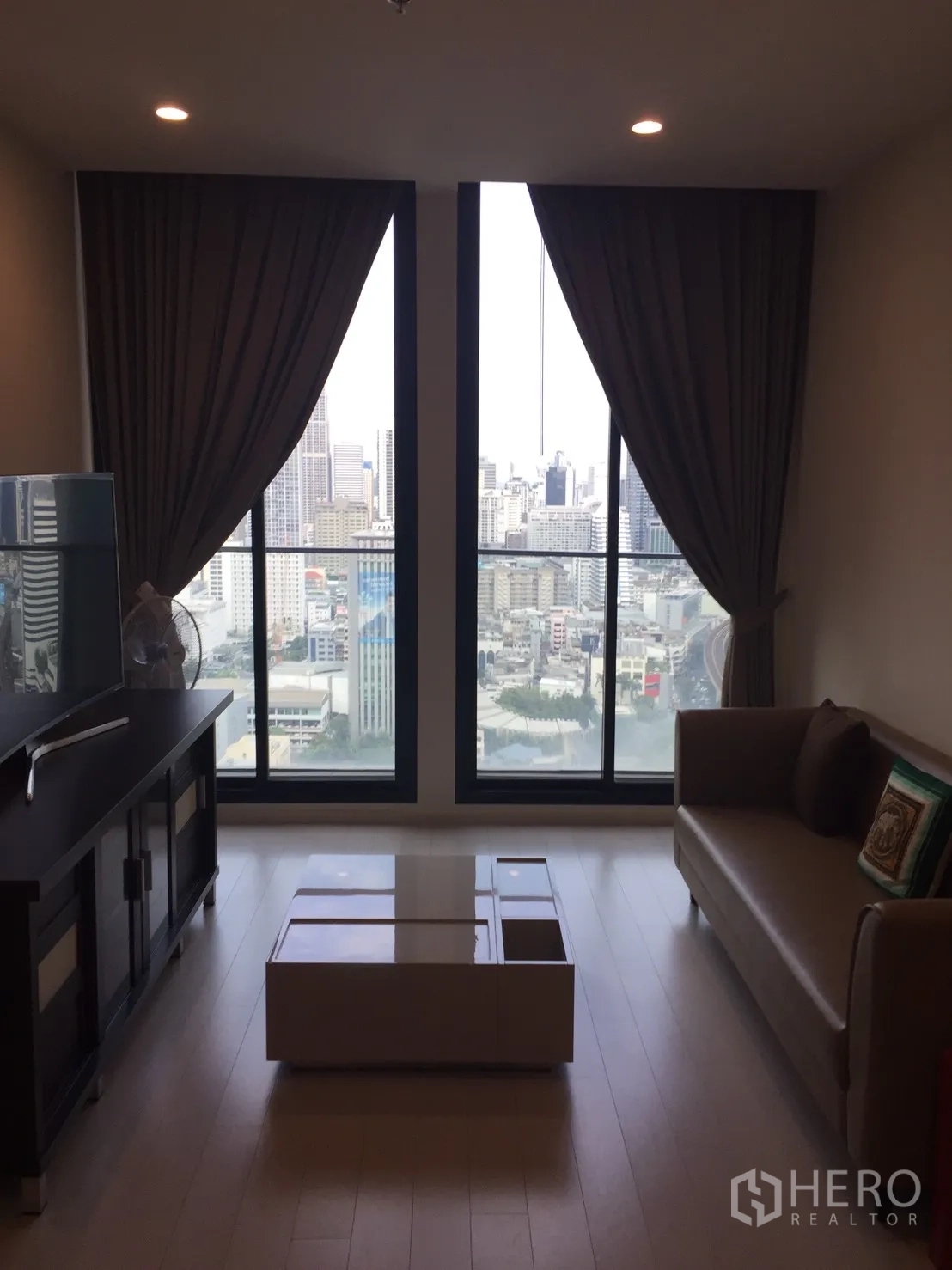 Condominium for rent in Pathum Wan, Bangkok - Living room with floor-to-ceiling windows, city skyline view, sofa, and coffee table.