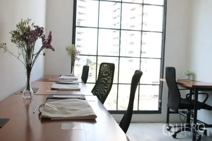 Office Space for rent in Khlong Toei, Bangkok - Row of workstations beside a floor‑to‑ceiling black‑frame window with city view, natural light and minimalist décor in a Thonglor office.