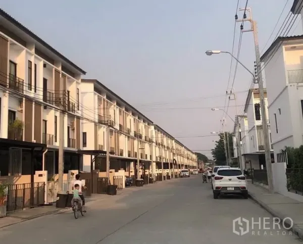 Townhouse for rent or sale in Bang Kapi, Bangkok - Row of modern three-storey townhouses along a wide internal street in a gated community.