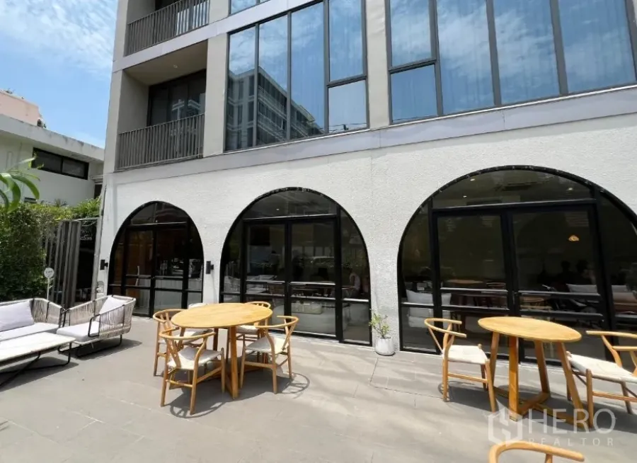 Retail Space for rent in Watthana, Bangkok - Modern building facade with arched black-framed glass doors opening to a sunny patio with round wooden tables.