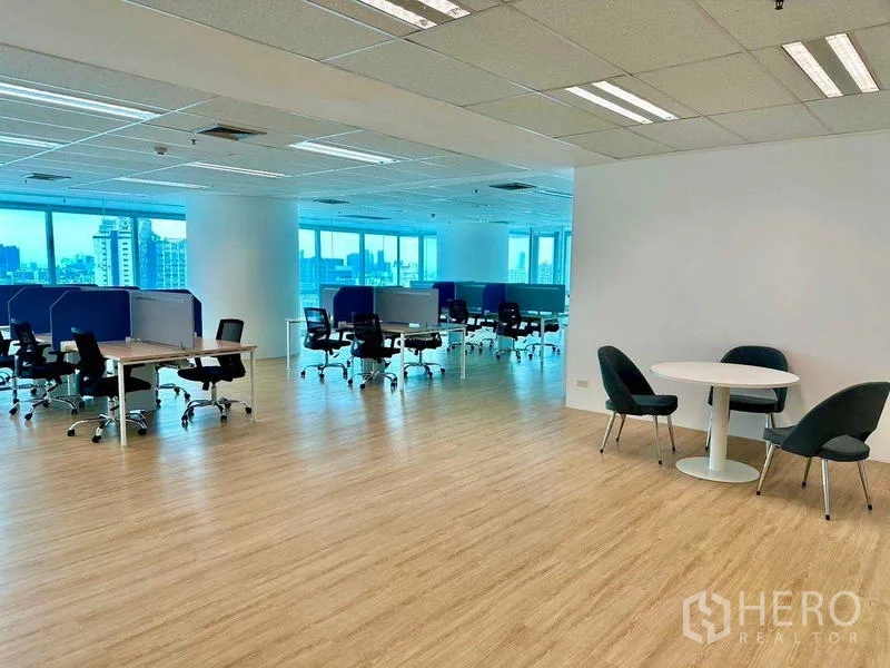 Office Space for rent - Spacious office floor with desk rows, a round collaboration table, and large windows with skyline views.