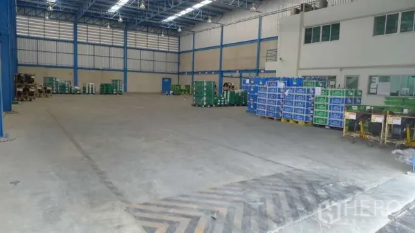 Warehouse for rent in Bang Phli, Samut Prakan - Open warehouse floor with stacked crates, adjoining office block, and marked loading zone.