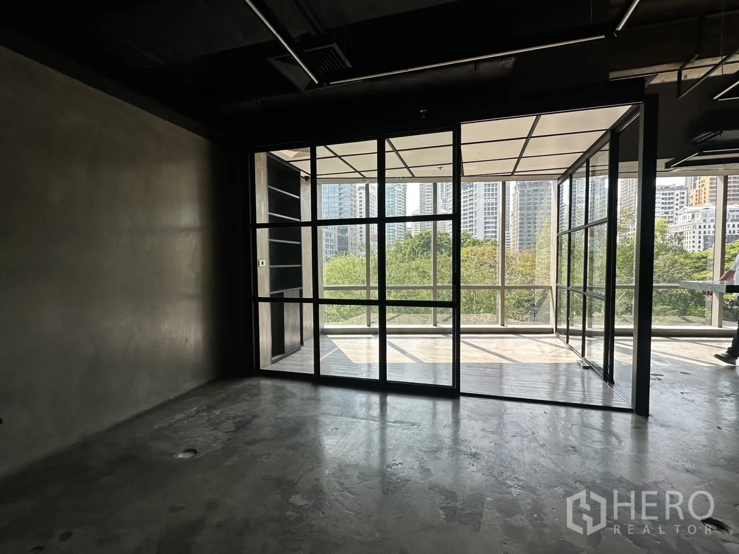 Office Space for rent in Pathum Wan, Bangkok - Empty room facing black-framed sliding glass doors and city views beyond greenery.