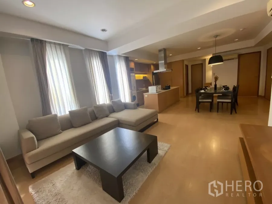 Condominium for rent in Watthana, Bangkok - Open-plan living room with L-shaped sofa, coffee table and tall curtained windows in a Bangkok condo.