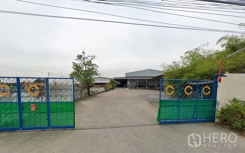 Warehouse for rent in Bang Phli, Samut Prakan - Gated warehouse entrance with a wide concrete driveway and metal-roof building set back in Bang Phli, Samut Prakan.