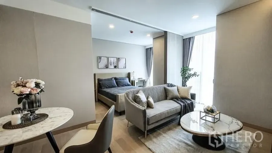 Condominium for sale in Khlong Toei, Bangkok - Another angle of the living room and bedroom divided by a sliding partition, grey sofa, and marble tables.