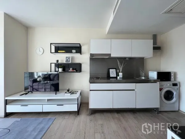 Condominium for rent in Khlong Toei, Bangkok - Open‑plan living and kitchen with white cabinetry, stainless countertop, microwave and washing machine.