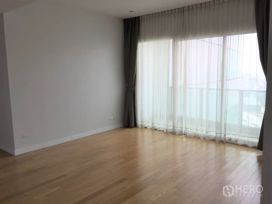 Condominium for rent in Khlong Toei, Bangkok - Bright living space with floor-to-ceiling windows and sheer curtains overlooking the city.
