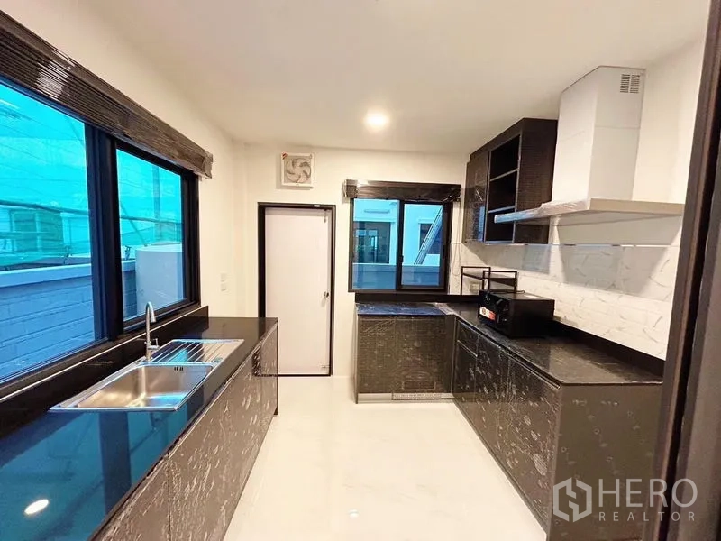 Detached House for rent in Bang Phli, Samut Prakan - Fitted kitchen with black stone countertops, cabinets, range hood and large windows.